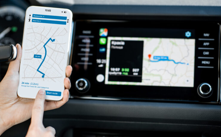 Close-up of a smartphone with navigation app in the modern car with monitor on the background